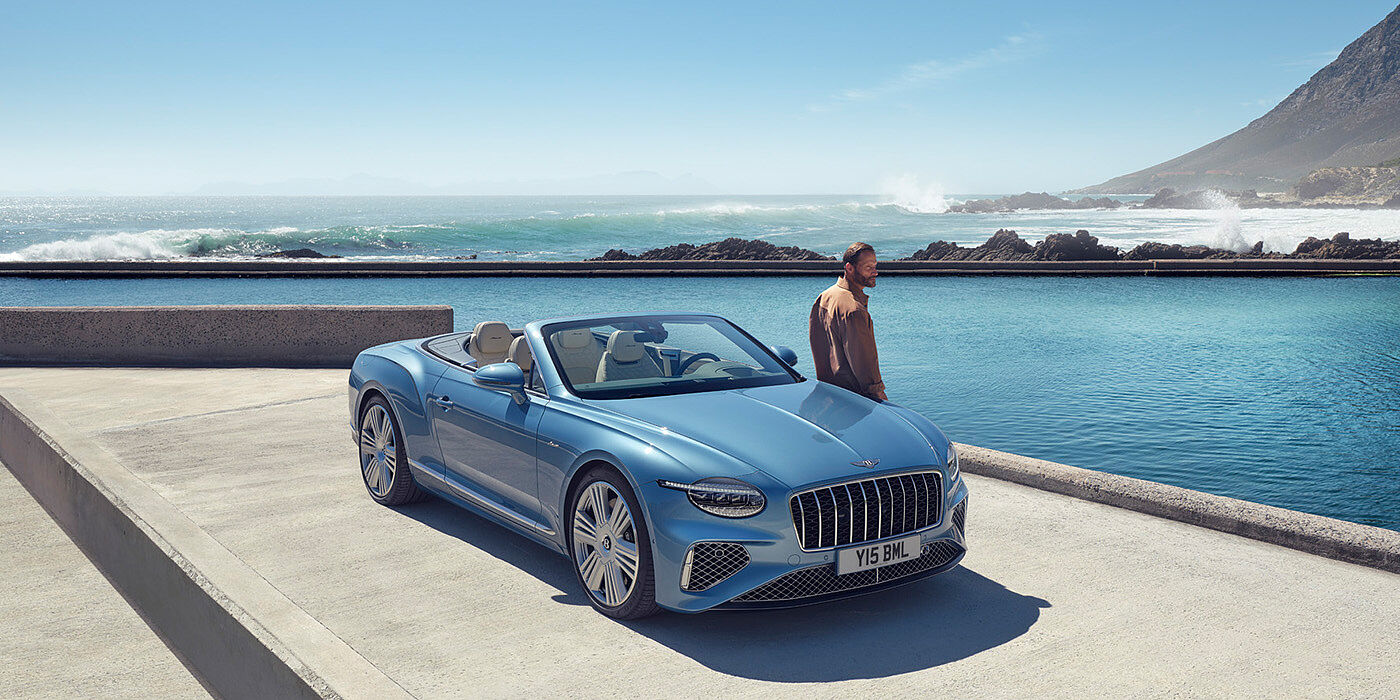 Bentley Doha New Bentley Continental GTC Azure convertible front view in Light Windsor blue paint with 22 inch ten spoke wheels parked by the sea in the sunshine

