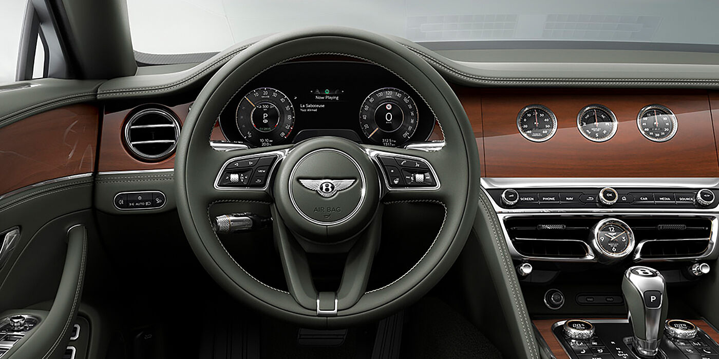 Bentley Doha New Bentley Flying Spur sedan front cabin in Cumbrian Green hide and Crown Cut walnut veneer showing steering wheel and Rotating Display with three clocks on face