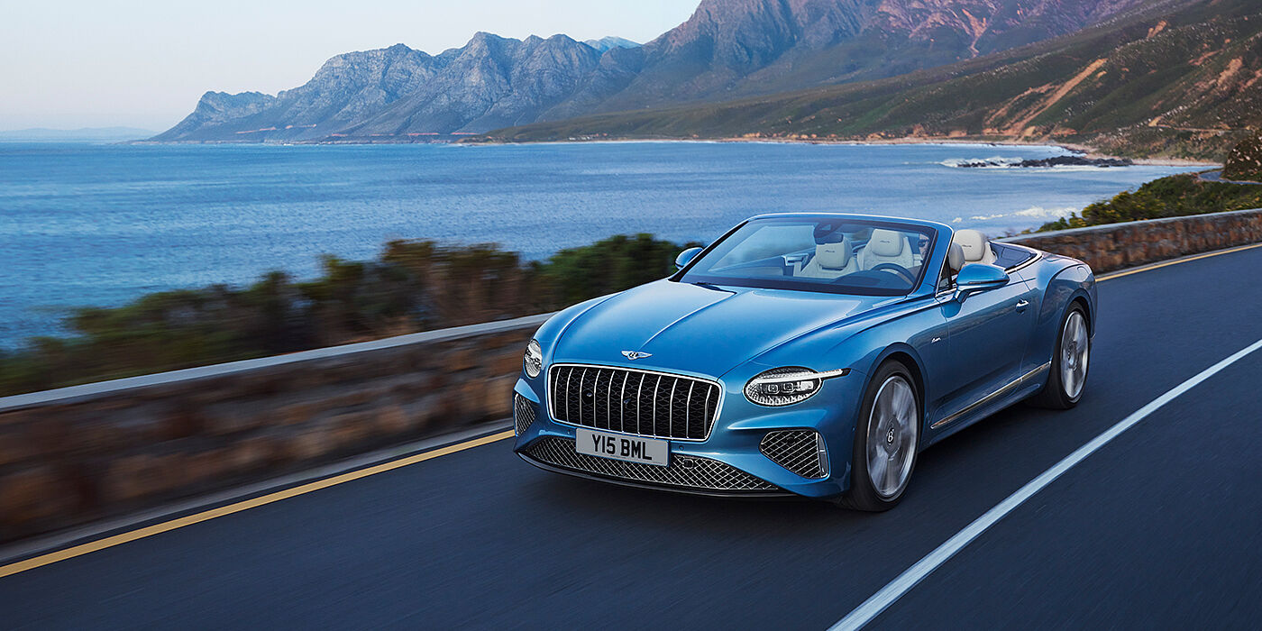 Bentley Doha New Bentley Continental GTC Azure convertible in Light Windsor blue paint with 22 inch Azure wheels and chrome grill, driving dynamically by the sea