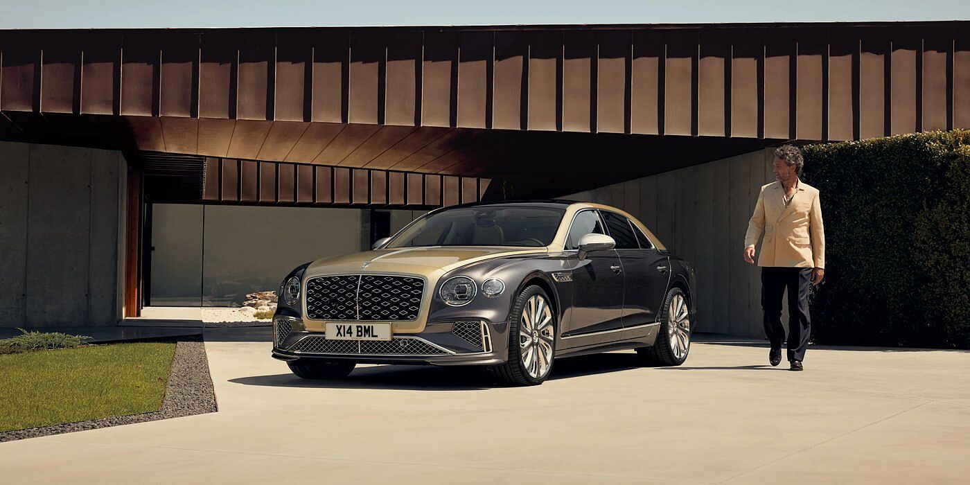 Bentley Doha Bentley New Flying Spur Mulliner V8 hybrid sedan front three quarters in Rose Gold over Magnetic paint, parked near modern home