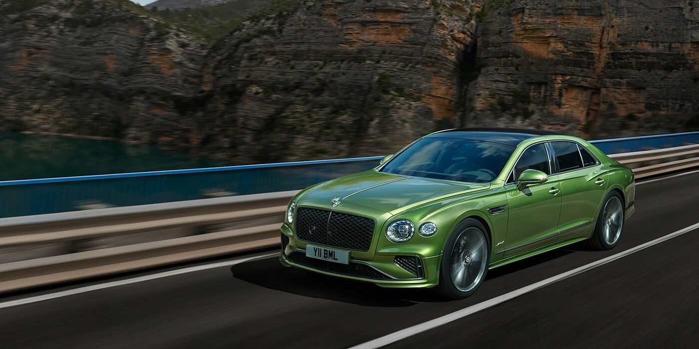 Bentley Doha Bentley New Flying Spur Speed v8 hybrid sedan driving dynamically on a mountain road in Tourmaline Green paint