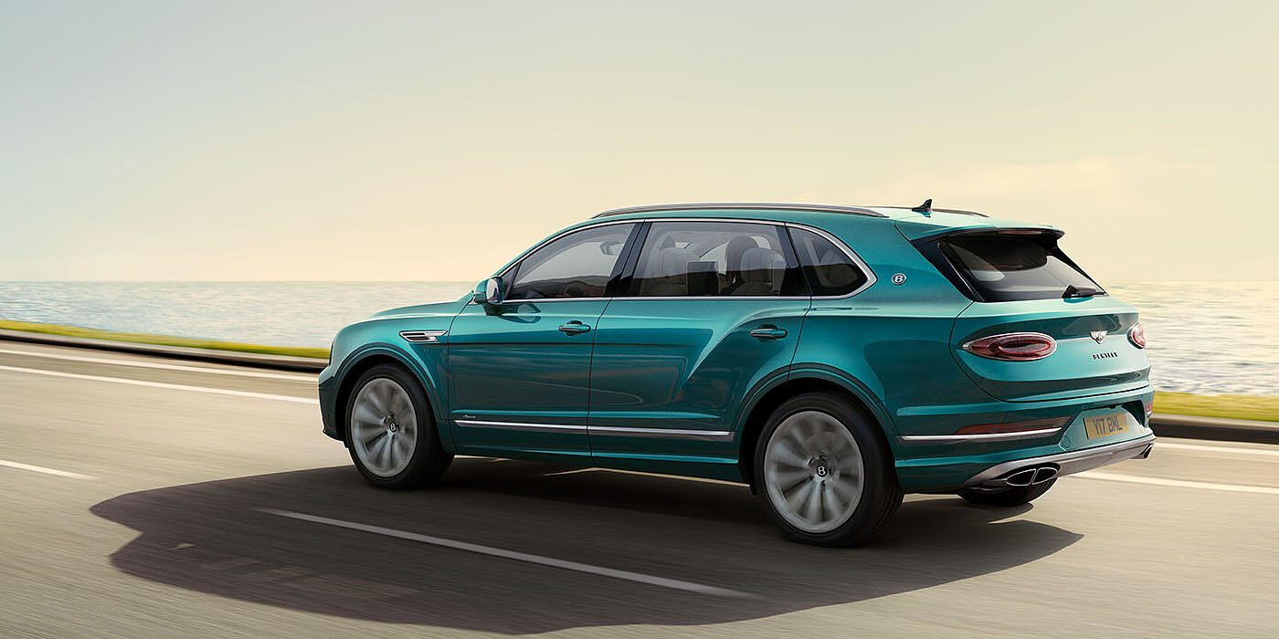 Bentley Doha Bentley Bentayga Extended Wheelbase Azure luxury SUV rear three quarter in Topaz Blue by Mulliner paint, driving on an ocean road.