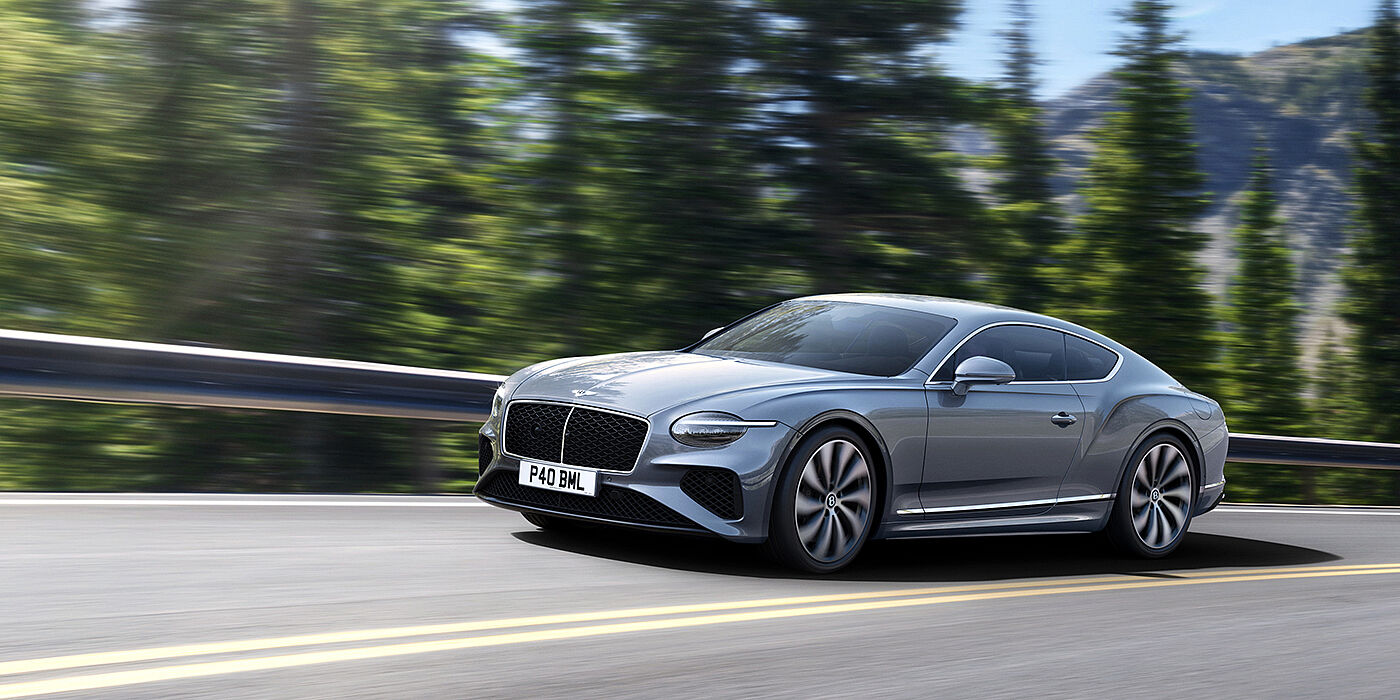 Bentley Doha New Bentley Continental GT coupe in Silverlake paint and 22 inch ten-spoke wheels, driving dynamically on a tree-lined road in the sunshine