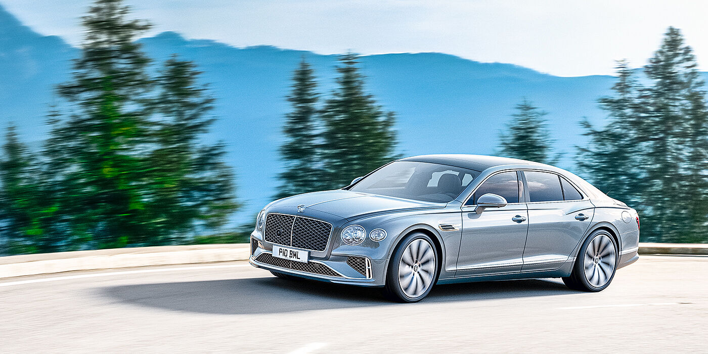 Bentley Doha New Bentley Flying Spur sedan side view in Silverlake paint with ten spoke wheels and chrome matrix grille driving dynamically on a mountain road