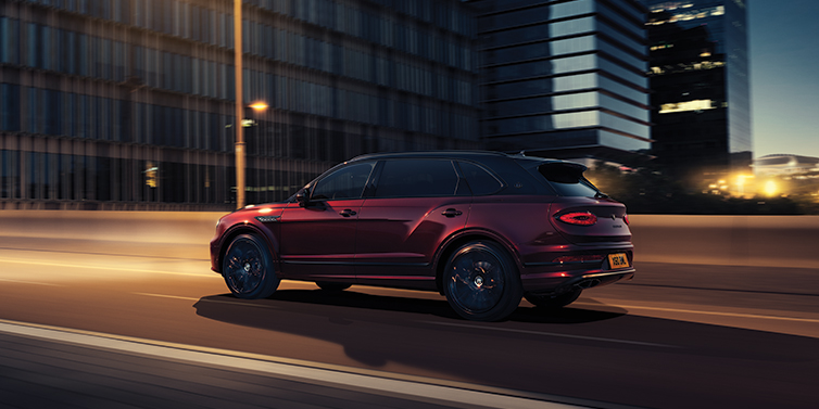 Bentley Doha Bentley Bentayga Extended Wheelbase Mulliner SUV in Cricket Ball red paint driving dynamically in city at night